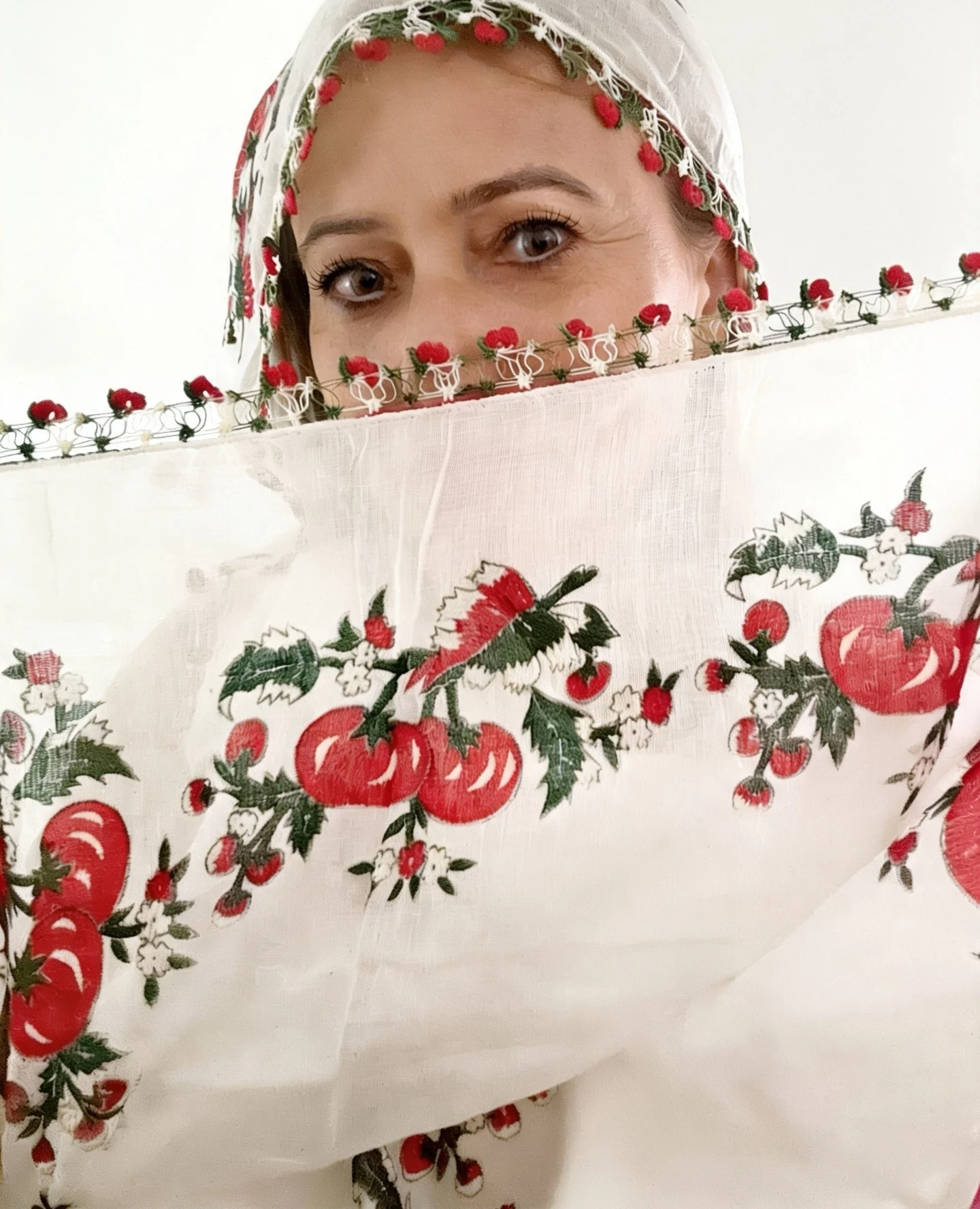 Ayten holding a white scarf embroidered with red cherries and edged with oya, close to her face