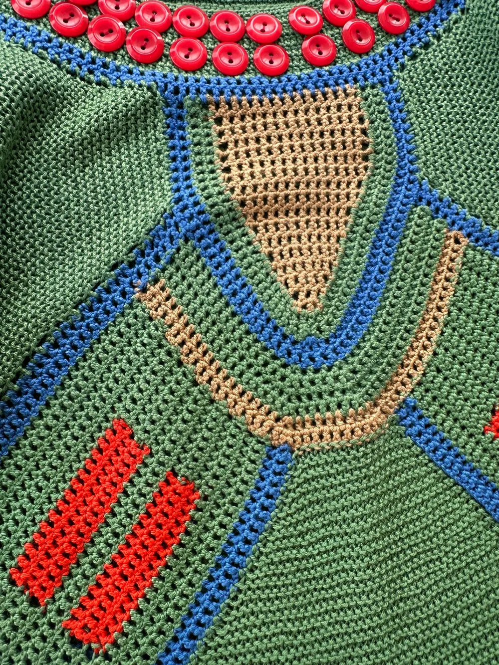 Close-up of the green crocheted dress, with red buttons and geometric motifs in blue, coral and sand
