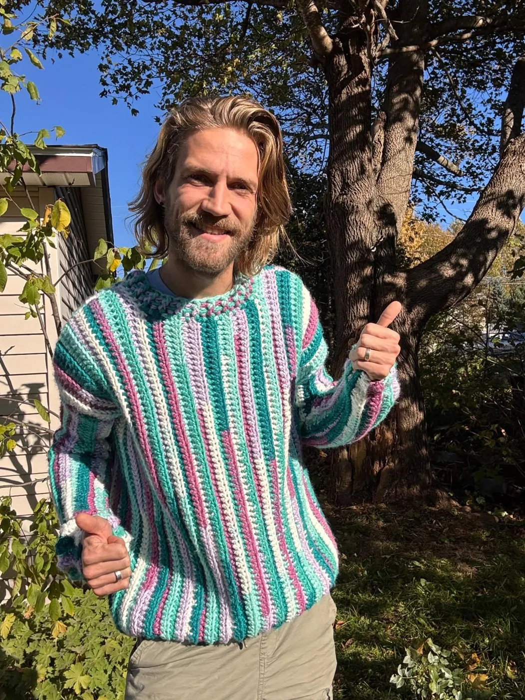 Vic giving a thumbs up in a crocheted jumper with mint, teal, lilac and white vertical stripes