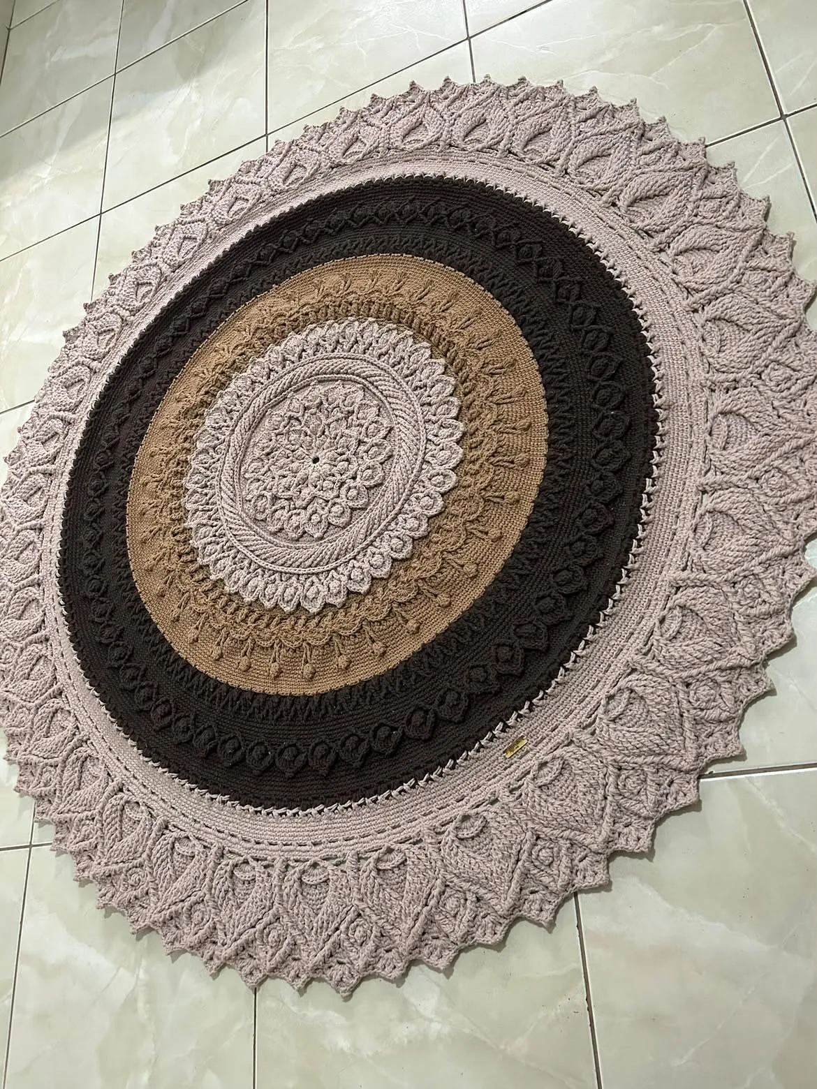 Large round crocheted rug in pale pink, dark brown and sand, with a textured border of leaf motifs
