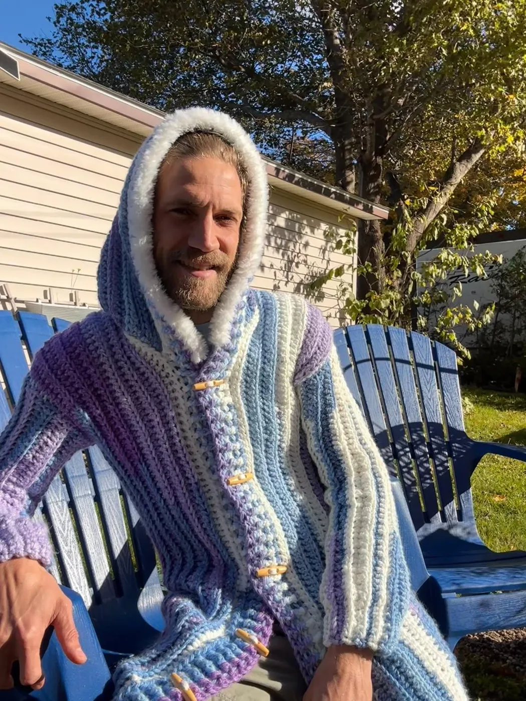 Vic in a long hooded crocheted coat in blue, lilac and white, with wooden toggles