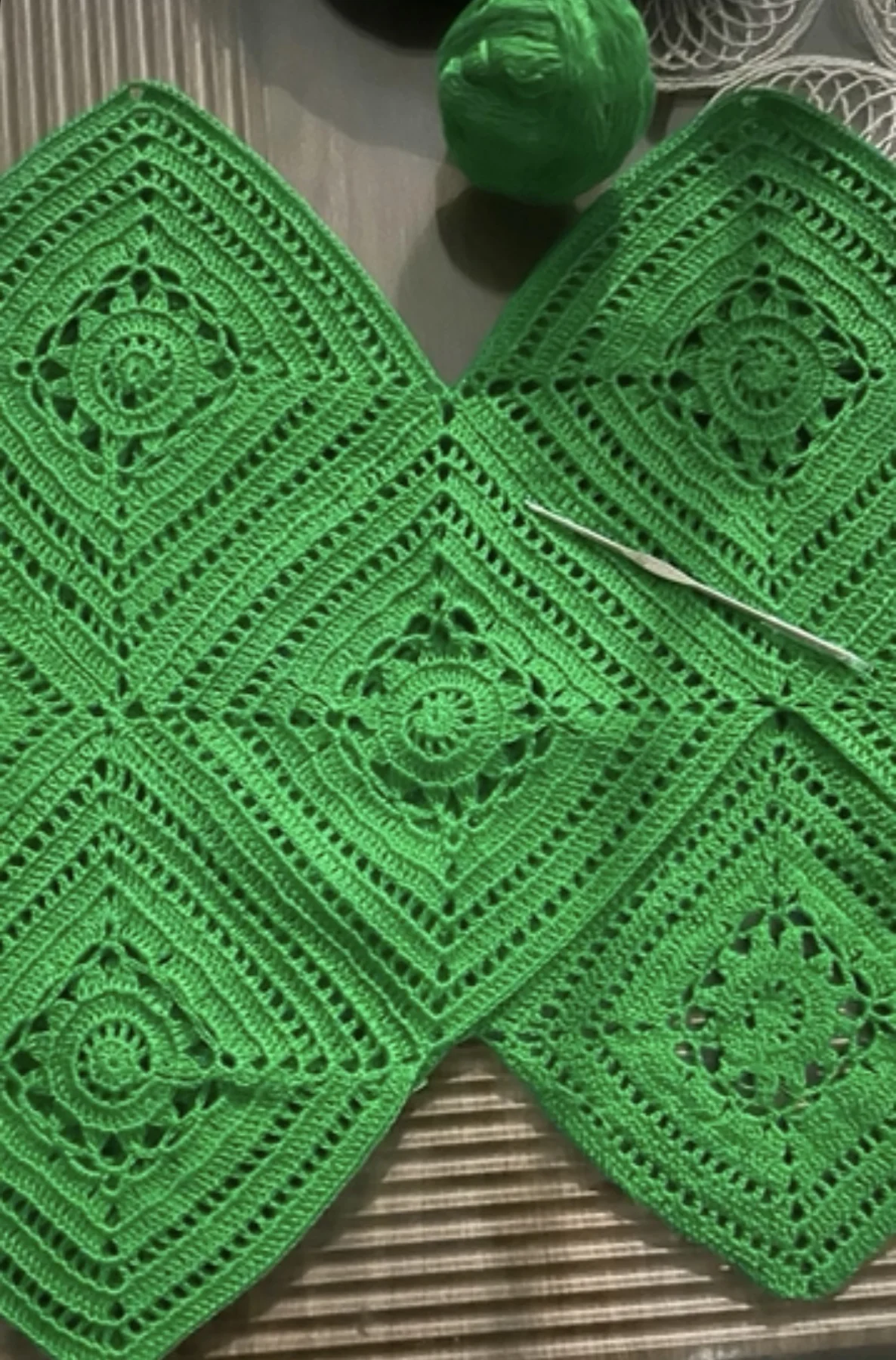 Green crocheted squares joined together, with a steel hook and a ball of green thread